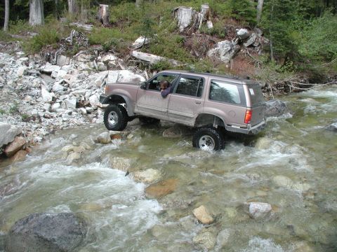 Lifted tan SUV driving through a rocky river.