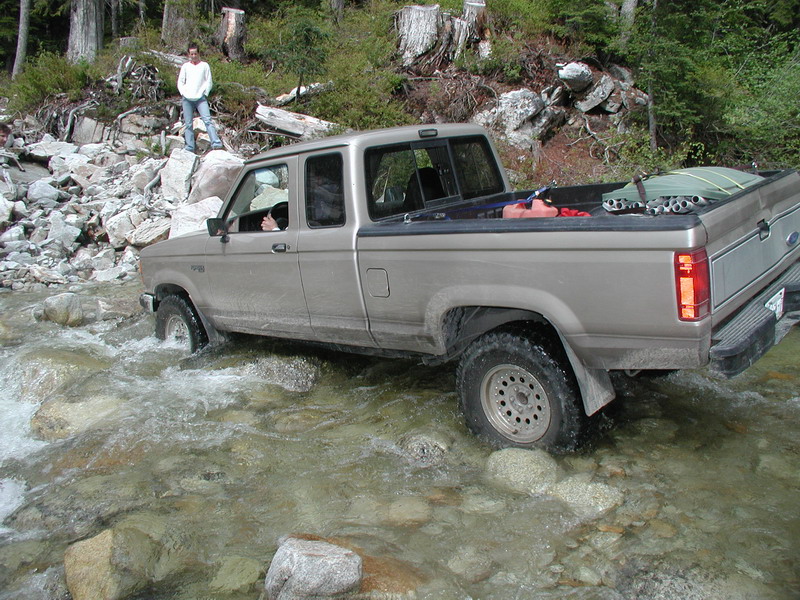 Tan Ford pickup truck driving through a rocky stream.