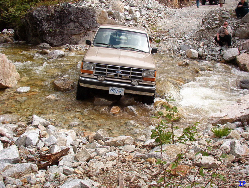 Tan Ford pickup truck driving through a rocky stream.