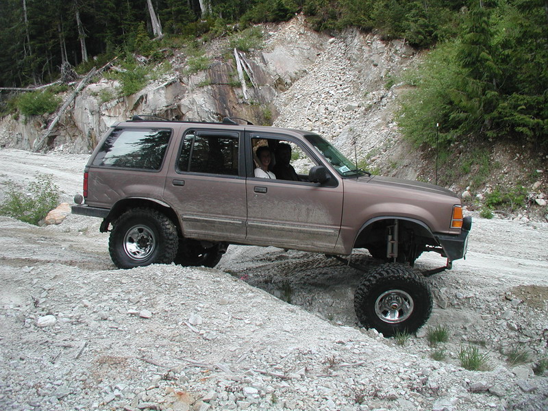 Lifted brown Ford Explorer off-roading on a rocky trail.