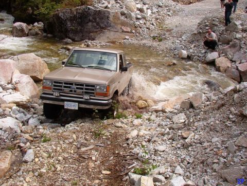Tan Ford pickup truck driving through a rocky stream.
