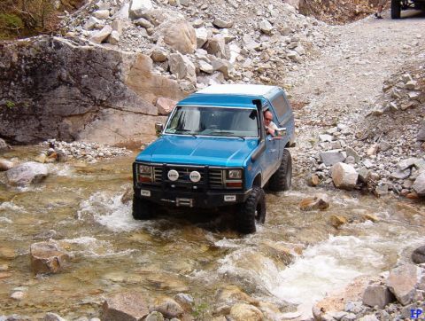 Blue 1980s Ford Bronco driving through a rocky river with a snorkel.