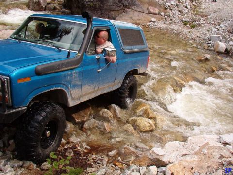 Blue Ford Bronco driving through a rocky stream with a snorkel.