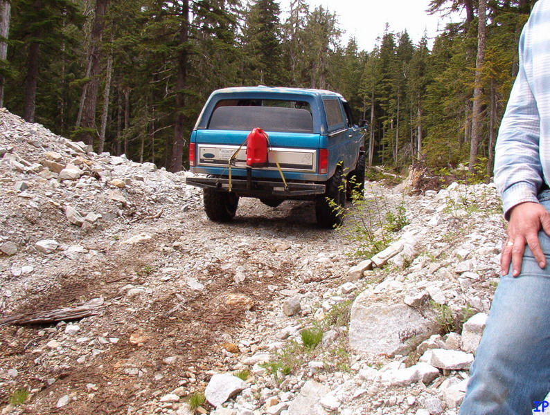 Rear view of a blue 1985 Ford Bronco on a rocky trail with a red gas can on the back.