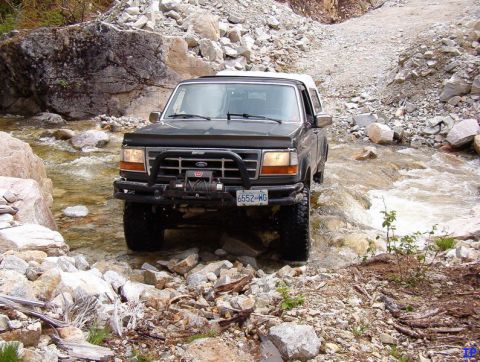 Dark Ford Bronco driving through a rocky stream.