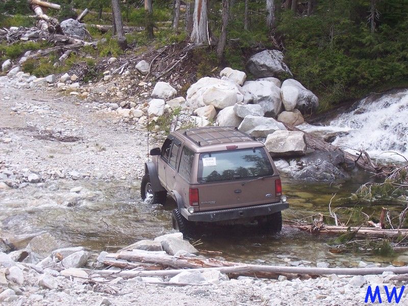Brown SUV driving through a rocky stream near a waterfall.