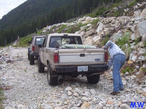 Tan Ford pickup truck on a rocky trail with a person in the bed.