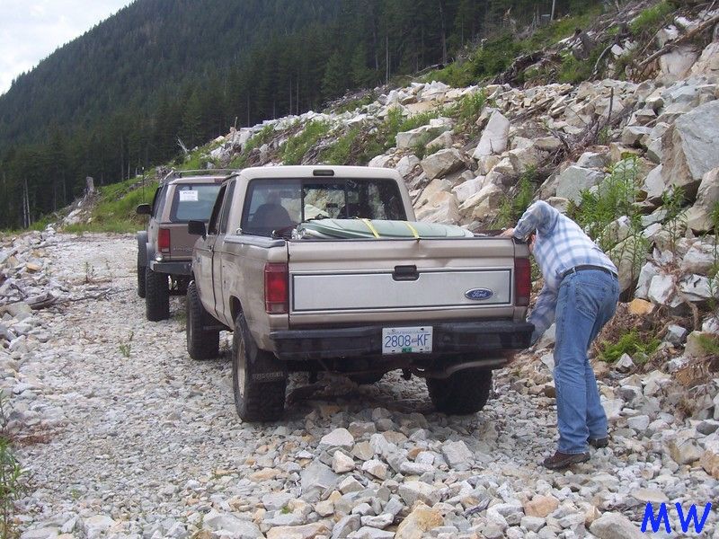 Tan Ford pickup truck on a rocky trail with a person in the bed.