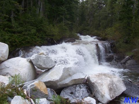 Waterfall in a forest with large boulders in the foreground.