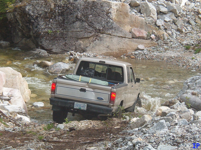 Tan Ford pickup truck driving through a rocky river.