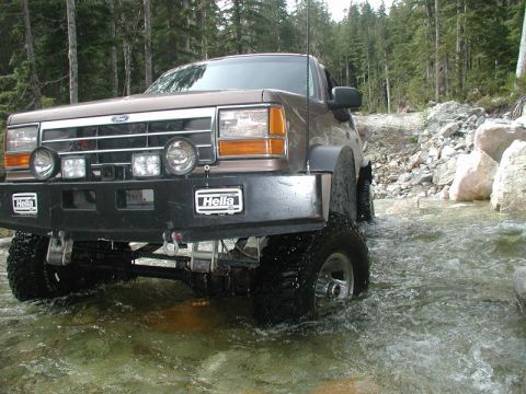 Lifted brown Ford Explorer driving through a stream in a forest.