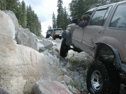 Brown SUV on a rocky off-road trail with other vehicles.