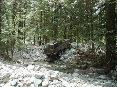 Brown SUV stuck in a rocky streambed in a forest.