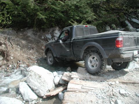 Black pickup truck driving through a rocky stream.