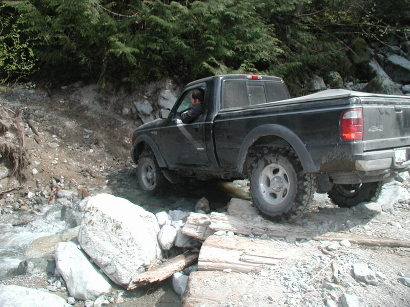 Black pickup truck driving through a rocky stream.