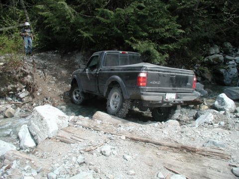 Black Ford Ranger pickup truck driving through a rocky stream.