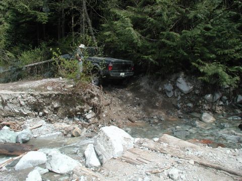 Person standing next to a black pickup truck on a damaged road.