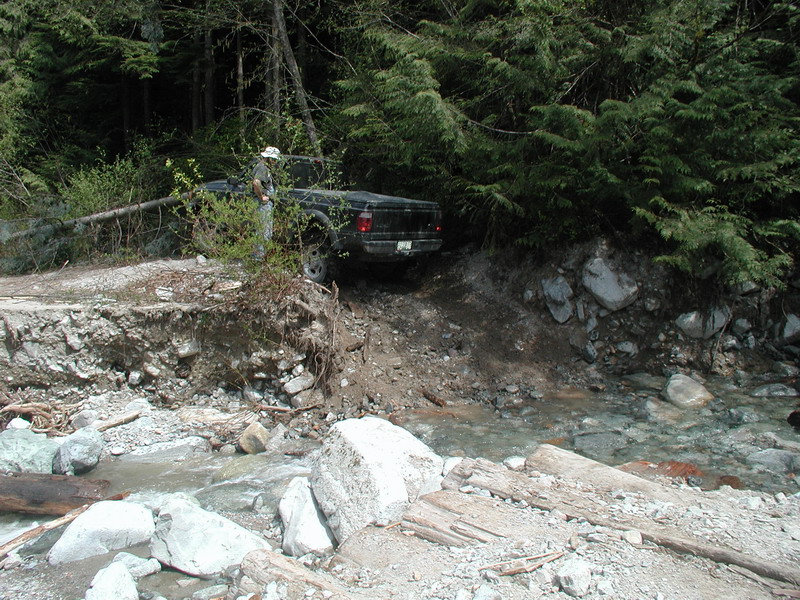 Person standing next to a black pickup truck on a damaged road.