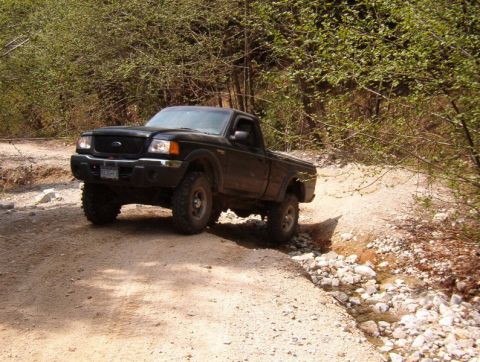 Black Ford Ranger pickup truck on a rocky off-road trail.