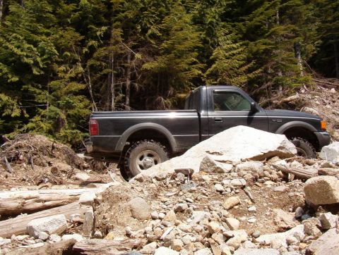 Dark pickup truck on a rocky forest trail.