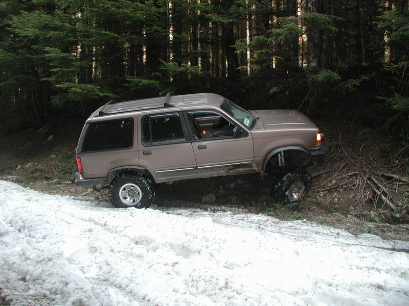 Lifted tan Ford Explorer on a snowy forest trail.