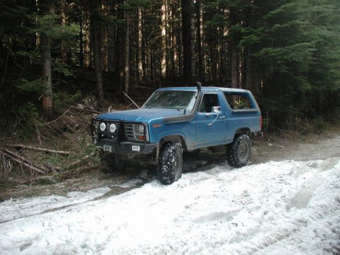 Blue Ford Bronco with off-road modifications on a snowy forest trail