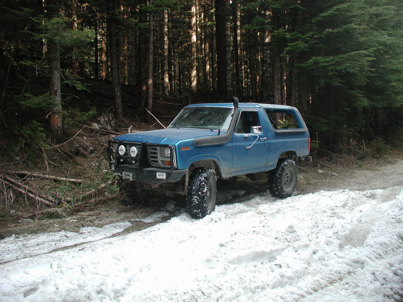 Blue Ford Bronco with off-road modifications on a snowy forest trail