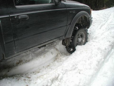 Black pickup truck stuck in deep snow, front passenger side tire visible.