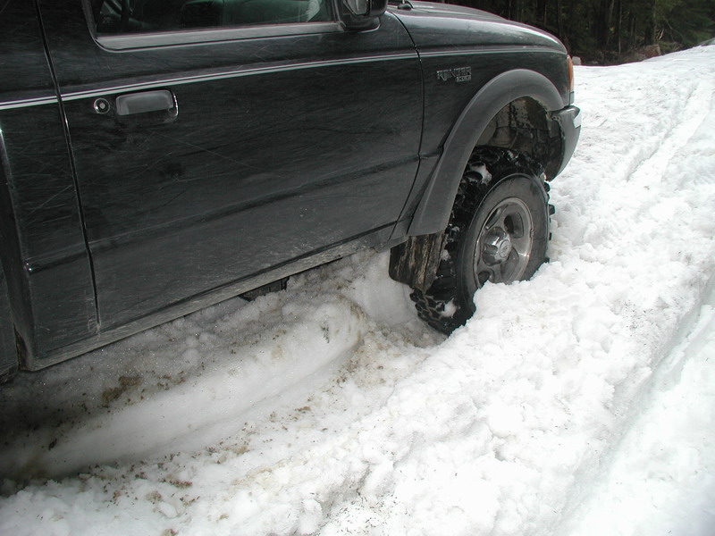 Black pickup truck stuck in deep snow, front passenger side tire visible.