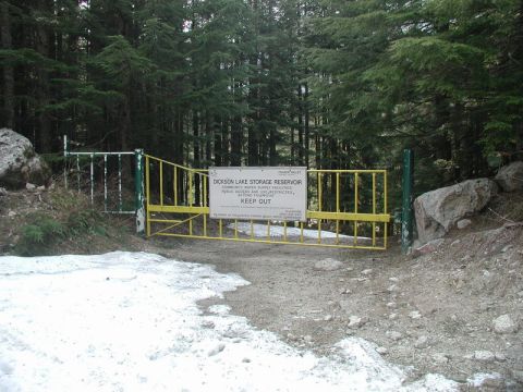 Yellow gate with a sign blocking a forest road.
