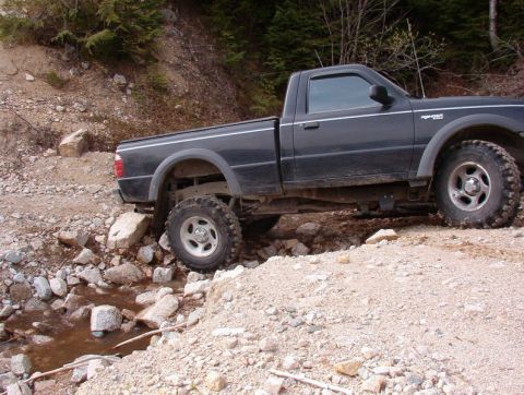 Dark pickup truck with off-road tires driving through a rocky stream.