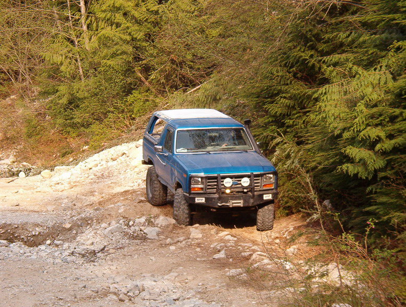 Blue 1985 Ford Bronco on a rocky trail with trees