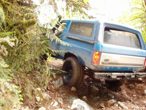 Blue Ford Bronco off-roading on a rocky, wooded trail.
