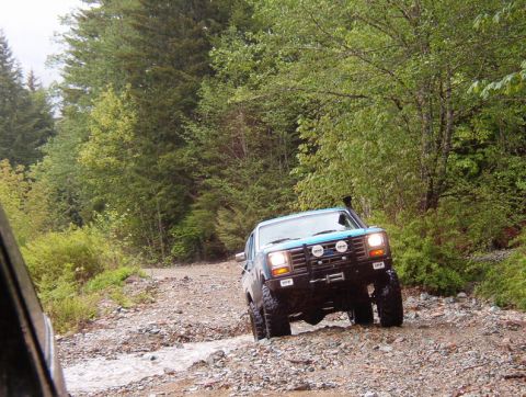 1985 Ford Bronco on a rocky, wet forest trail