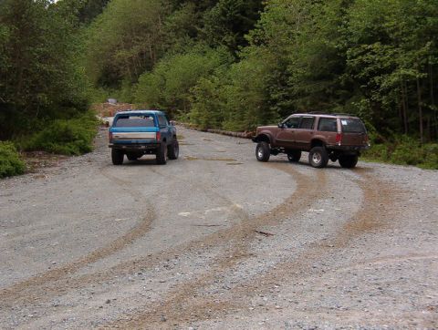 Blue pickup truck and brown SUV on a gravel road in a forest.