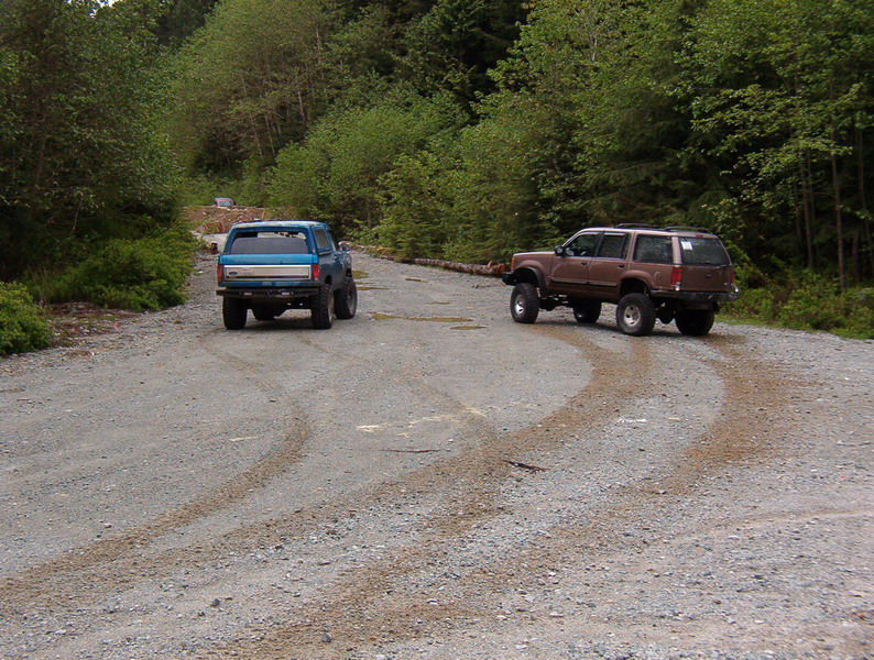 Blue pickup truck and brown SUV on a gravel road in a forest.