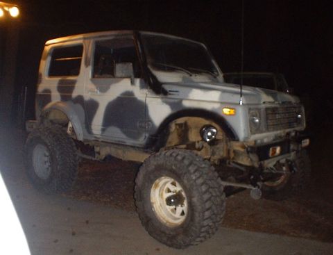 1989 Ford Bronco - A camouflaged Suzuki Samurai is parked at night, equipped with large off-road tires and an aftermarket bumper.
