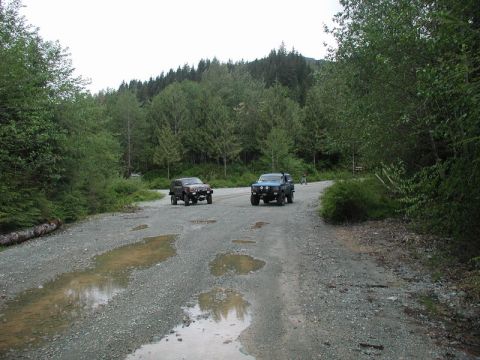 Two SUVs on a gravel road in a forest.