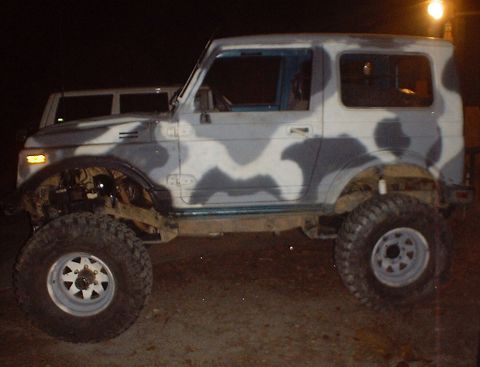 1989 Ford Bronco - A modified Suzuki Samurai with camouflage paint and off-road tires is shown parked outdoors at night.