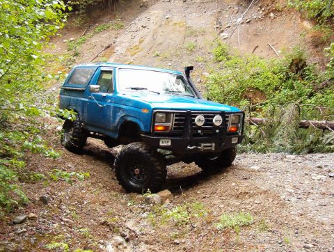 Blue 1980s Ford Bronco with off-road tires and snorkel on a dirt trail.