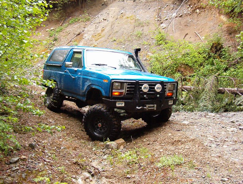 Blue 1980s Ford Bronco with off-road tires and snorkel on a dirt trail.