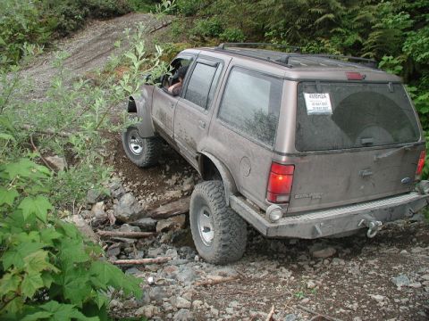 Brown Ford Explorer off-roading on a rocky trail, front passenger side lifted.