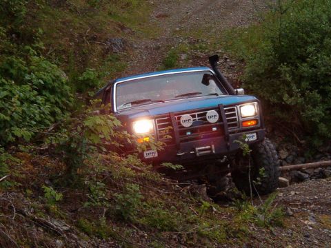 Blue Ford Bronco off-roading on a steep, wooded trail.