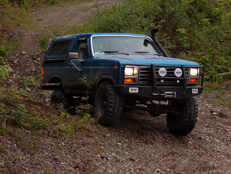 Blue Ford Bronco off-roading with large tires, winch, and snorkel.