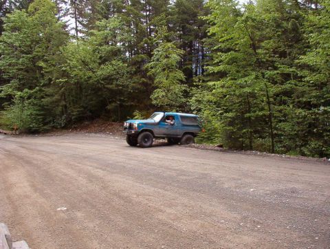 Blue Ford Bronco on a dirt road in a forest.