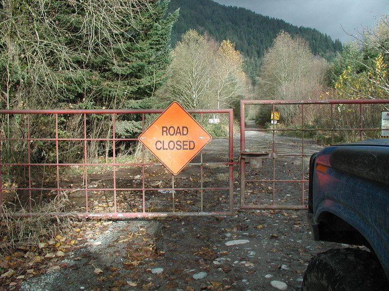 Blue Ford Bronco parked in front of a closed gate with a road closed sign.