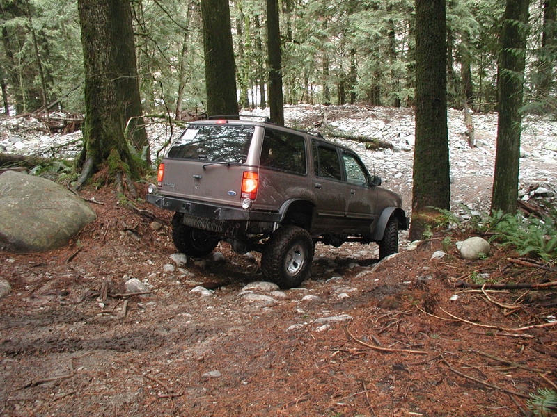 Lifted brown SUV on a rocky, wooded trail.