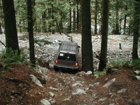 Brown SUV driving on a rocky, wooded trail.