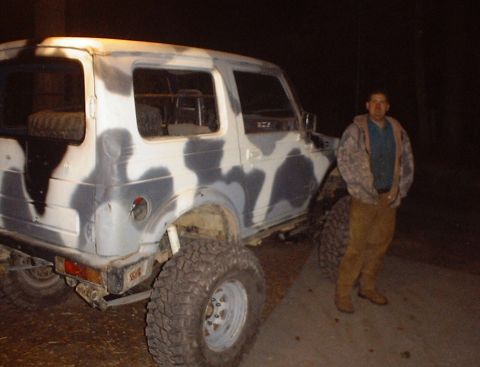 1989 Ford Bronco - A man stands beside a camouflaged Suzuki Samurai with oversized tires.
