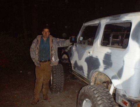 1989 Ford Bronco - A man poses next to a camouflage-painted SUV, which appears to be a Suzuki Samurai.
